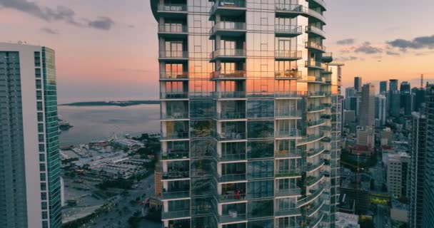 アトランティックな海とフェリスホイールの遊歩道の背景から日没の中心にあるマイアミのガラス高層ビル 空の窓からの反射 夜の街と家を眺める — ストック動画