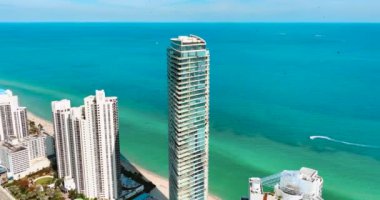 Miami Plajı. Tekneli ve dalgalı turkuaz su. Atlantik Okyanusu 'nun arka planında daireleri olan lüks otellerden oluşan yüksek cam binalar. Hava görünümü.