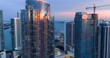 Günbatımında Miami 'de cam gibi modern binalar. Okyanusun arka planında akşam parlayan şehir manzarası. Pencerelerdeki yansımalar.