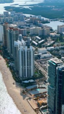 Panorama, oteller, sokaklar, körfez ve şemsiyeli kumlu Miami plajı manzarası. Okyanusun turistik kıyı şeridi. Dikey video.