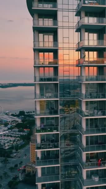 日落时分 迈阿密市中心的玻璃摩天大楼在大西洋的背景下与摩天轮共进 天空中的反光 夜市与房屋的空中景观 垂直录像 — 图库视频影像