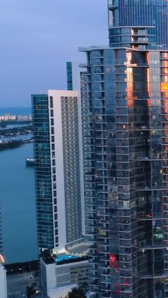 サンセットでマイアミのガラス高層ビル 夕暮れは窓の街を映し出しています バーティカルビデオ — ストック動画