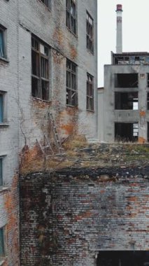 Terk edilmiş eski bir fabrikanın hava manzarası. Kırık pencere ve kapılar. Dikey video.