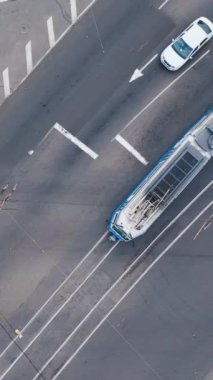 Şehirde büyük bir kavşak var. Arabalar, tramvaylar kesişiyor. Şehir ulaşımının otomobil trafiği, insansız hava aracı üst görüntüsü. Dikey video.