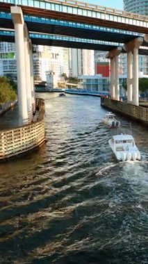 Miami, Florida, ABD - 05 Ocak 2024: Motorboat Miami şehir merkezindeki karayolu köprüsünün altında nehirde yüzüyor. Hava görüntüsü. Miami nehri üzerinde köprüleri olan insansız hava aracı uçuşu. Dikey video.