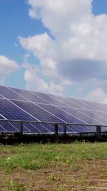 Elektrik üretimi için fotovoltaik güneş panelleri. Yeşil bir alanda güneş enerjisi santrali. Bulutlu gökyüzü. Dikey video.