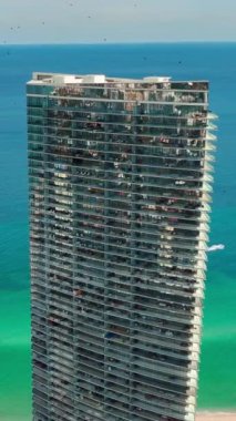 Atlantik Okyanusu 'nun turkuaz su arka planına karşı otel binasının cam cephesi. Sunny Isles Sahili hava manzarası. Dikey video.