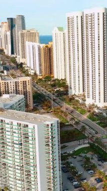 Sunny Isles Beach Florida 'daki yüksek binaların tepeleri. Collins Bulvarı 'nda arabalı. Okyanus kıyısında daireleri var. Dikey video.