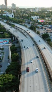 Miami, Florida, ABD - 05 Ocak 2024: 95 nolu otoban üzerinde yoğun trafik ile uçuş. Gün batımında şehir merkezinde arabalar. Küçük evleri ve yeşil ağaçları olan şehir merkezinde. Dikey video.