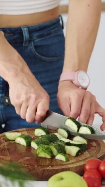 Salata için yeşil bir salatalığı tahta bir tahtanın üzerinde bıçakla kesmek. Vejetaryen yemek hazırlığı. Dikey video.