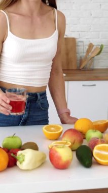 Mutfaktaki kız taze meyve suyu içiyor. Sağlıklı beslenmek için meyve ve sebzeli bir masa. Dikey video.