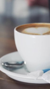 Ahşap masada hazır kapuçino ile beyaz bardak ve barmen başka bir fincana süt döküyor. Dikey video.