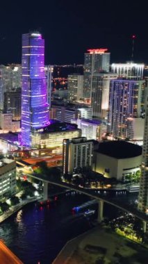 Miami, Florida, ABD - 05 Ocak 2024: Parlak ışıklarla Gece Şehri 'nin havadan görünüşü. Şehir merkezindeki gökdelenler, köprüler ve nehirler. Dikey video.