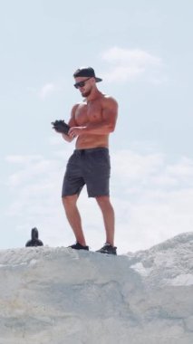 Güçlü bir adam açık hava antrenmanında şişeden su içer. Mavi gökyüzüne karşı beyaz bir dağda atlet. Dikey video.