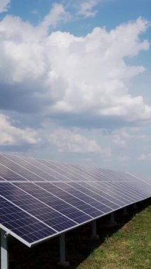 Yeşil alandaki uzun güneş panelleri bulutlu mavi gökyüzüne karşı. Güneş enerjisi istasyonu. Dikey video.