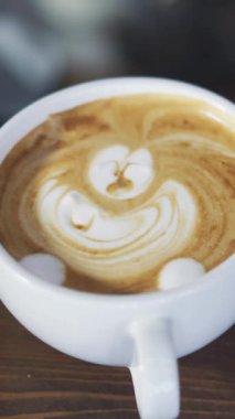 Beyaz bir bardak kapuçinonun içine sopa çizilmiş bir barmenin elleri. Güzel bir sabah kapuçino kahvesi yapma süreci. Dikey video.