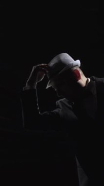 Takım elbiseli adam şapkasını takar ve dans etmeye başlar. Konser salonunun karanlık sahnesinde, Soffit 'in arka ışığında dansçı. Dikey video.