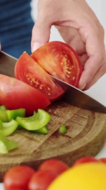 Kız, salata için mutfak tahtasındaki kırmızı domatesleri vejetaryen yiyecekler için sebzelerle dilimliyor. Dikey video.