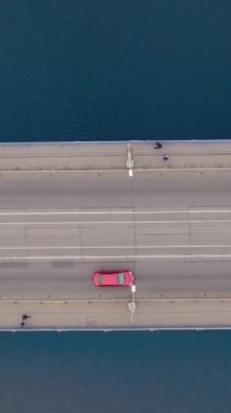 Tramvaylı hava köprüsü, hareket eden arabalar. İnsansız hava aracı köprüde nehirle uçuyor, bir otoyolda yolculuk yapıyor. Dikey video.