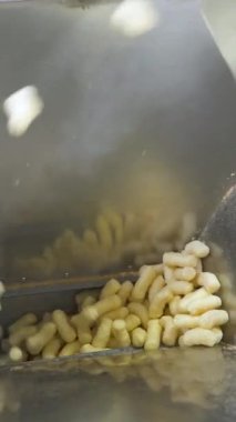 Yiyecek fabrikasındaki metal bir konteynıra abur cubur dökmek. Ürünler için otomatik paketleme hattı. Dikey video.