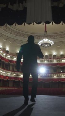 Sahneye mikrofonlu bir sanatçının silueti giriyor. Çorapların ışığında boş bir oditoryum. Dikey video.