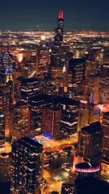 Gece vakti Chicago gökdelenleri. Güzel gökyüzünün arka planındaki çarpıcı gökdelenler boyunca insansız hava aracı görüntüleri yükseliyor. Dikey video.