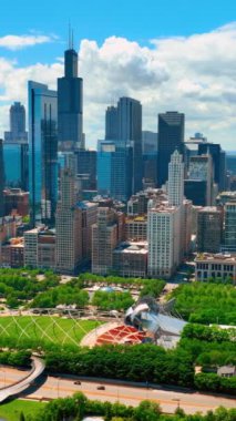 Chicago şehir merkezinde yeşil ağaçları ve çimenleri olan bir park. Uzun gökdelenler ve tarihi binalar. Hava görüntüsü. Dikey video.