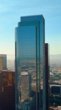 Los Angeles, CA, ABD - 15 Eylül 2024: Pencerelerinde yansıması olan uzun camlı bir City National Bank. Şehir merkezinin havadan görüntüsü. Dikey video.