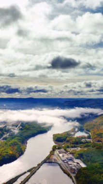Amerika 'da sonbaharda gündoğumunda alçak bulutlarda güzel kıvrımlı nehrin hava manzarası. Nehir vadisi sisli, güneş ışınları bulutların arasında. Dikey video.