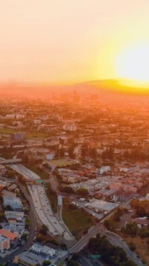 Ufukta batan büyük sarı güneş ışınları altında caddeleri, arabaları ve evleri olan Los Angeles şehri. Hava akşam manzarası. Dikey video.