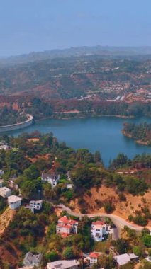 Hollywood Reservoir 'a yakın bir yerleşim yeri. Hollywood Hills, Los Angeles 'ta yamaçtaki güzel evlere tepeden bakıyor. Hava görüntüsü. Dikey video.