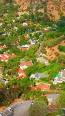 Outpost Estates, Los Angeles 'ın Hollywood Hills bölgesinde yer alan bir mahalledir. Yeşil ağaçların arasındaki konut binalarının çatıları. Dikey video.