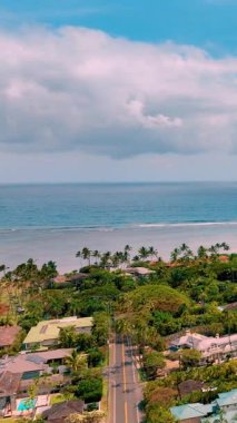 Sahildeki küçük yerleşim yerleri yeşil palmiye ağaçları arasında. Honolulu, Hawaii 'deki Kahala Sahili' nin havadan görüntüsü. Turkuaz sular, kumlu kıyılar ve dalgalı sular. Dikey video.