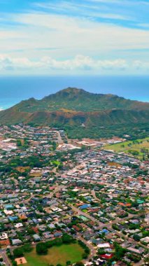 Yeşil bitki örtüsü olan Elmas Kafa volkanının dev krateri. Okyanus kıyısında evleri olan bir yerleşim yeri. Hava görüntüsü. Hawaii 'nin Oahu adası. Dikey video.