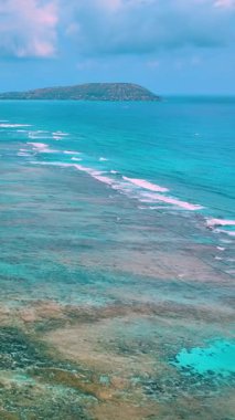 Hawaii, Oahu adasındaki turkuaz okyanus dalgalarıyla dolu kumlu bir sahil manzarası. Bir volkanın arka planına karşı kayalıklarla sığ bir kıyı. Dikey video.