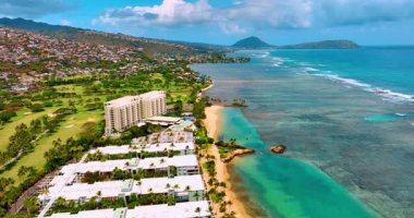 Kahala sahilindeki evlerin, resiflerin ve okyanus kenarındaki palmiye ağaçlarının havadan görünüşü. Sahilde turkuaz suyu olan lüks bir otel. Adanın volkanlı manzarası.