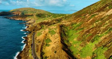 Turkuaz sular Oahu, Hawaii 'de kayalık bir kıyı şeridi ve kumlu bir plajla buluşur. Düz yeşil ve kahverengi tepeler boyunca uzanan dolambaçlı bir yol açık mavi gökyüzünün altında Koko krateri. Hava görünümü.