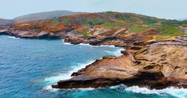 Dramatik kayalık uçurumları, canlı yeşil bitki örtüsü ve kıyıya vuran okyanus dalgalarıyla engebeli kıyı manzarası. Koko Krateri 'nin yamaçlarında. Sahildeki otoyol. Hava görünümü.