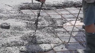 Metal takviye ağıyla bir temel tabakasına sıvı beton dök. İnşaat alanında çizmeli bir işçi. Otomatik yapı karışımı kaynağı.