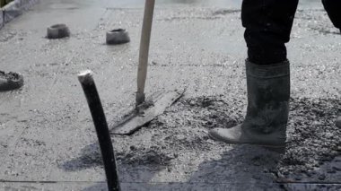 Döşemeyi metal tellerle döşemek. Beton döşeme üretimi. Dairenin zeminine baktık. Botlu bir işçi elle yüzeyi düzleştiriyor..