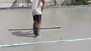 Elinde el aleti olan bir işçi bir inşaat alanındaki bir levhanın yüzeyine taze sıvı betonu düzleştirir ve düzleştirir..