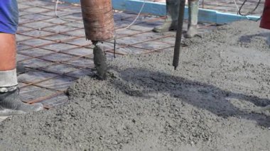 İnşaat işçisi pompa tübü ile çimento ya da beton döküyor. Güçlendirilmiş çelik çubuklar ve çubuklar. İşçilerin bacaklarına yakın çekim. Somut titreşim.