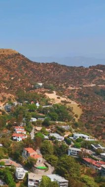 Los Angeles 'ta Hollywood tabelası olan dağın yamaçlarında ve eteklerinde ikamet eden binalar. Hava görüntüsü. Dikey video.