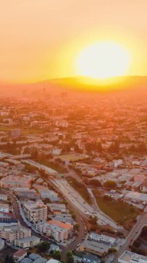 Gün batımında parlak güneş. Los Angeles şehrinin gökyüzü manzaralı evleri ve arabalı yolları var. Şehir merkezinde. Dikey video.