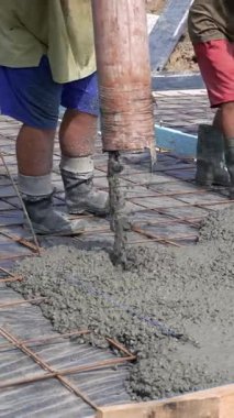 İşçiler beton döşemeli bir evin zeminine borudan çimento dökerler. İnşaat alanında ahşap işçiliği. Dikey video.