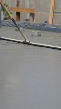 İnşaatçı, inşaat alanına dökülen taze, ıslak beton yüzeyini elle düzleştirir. Yumuşak bir alete yakın çekim. Dikey video.