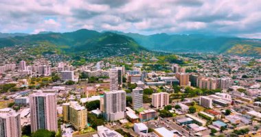 Güneşli bir günde Honolulu şehir merkezinde ikamet yeri. Waikiki bölgesinden hava görüntüsü. Bulutlu gökyüzüne karşı ormanlarla kaplı dağlar.