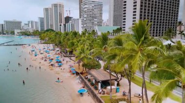 Yüksek binaları, palmiyeleri ve mavi suları olan Waikiki sahilinin havadan görünüşü. Honolulu, Hawaii. İnsanlar dinleniyor, güneşleniyor ve yüzüyor..