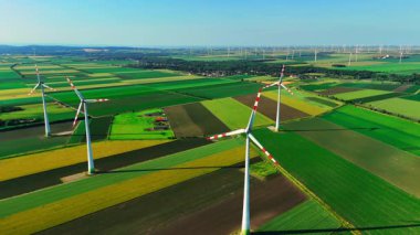 Avusturya 'daki renkli alanlar arasında yeşil, yenilenebilir, enerji veya elektrik için birçok rüzgar türbini veya rüzgar türbini bulunuyor. Tarım alanları ve enerji santralinin panoramik hava görüntüsü.