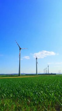 Açık mavi gökyüzüne karşı yeşil bir alanda büyük rüzgar türbinleri. Avusturya 'da enerji üretimi. Dikey video.